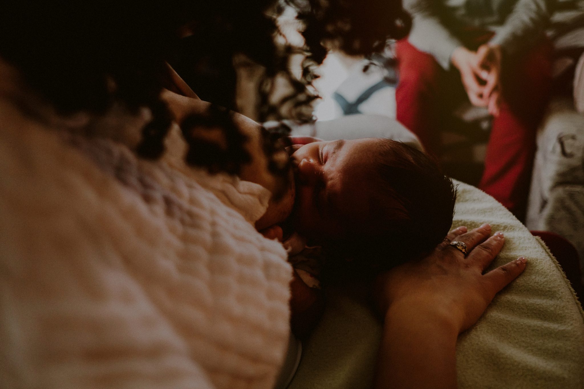 newborn baby breastfeeding with father in the background