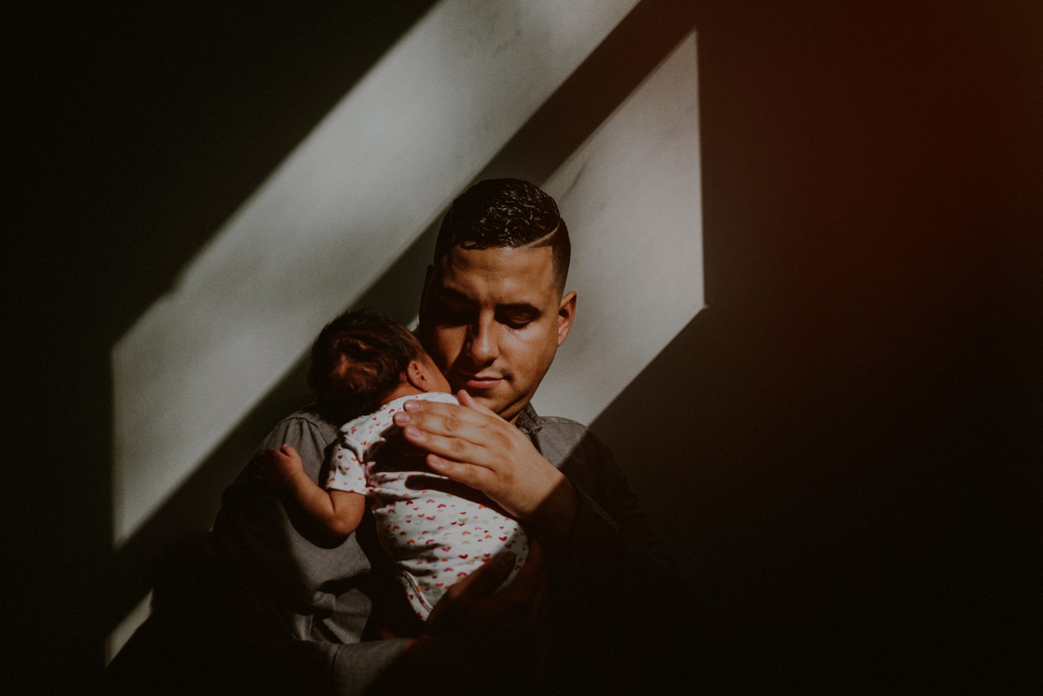 father tenderly holding baby in natural window light