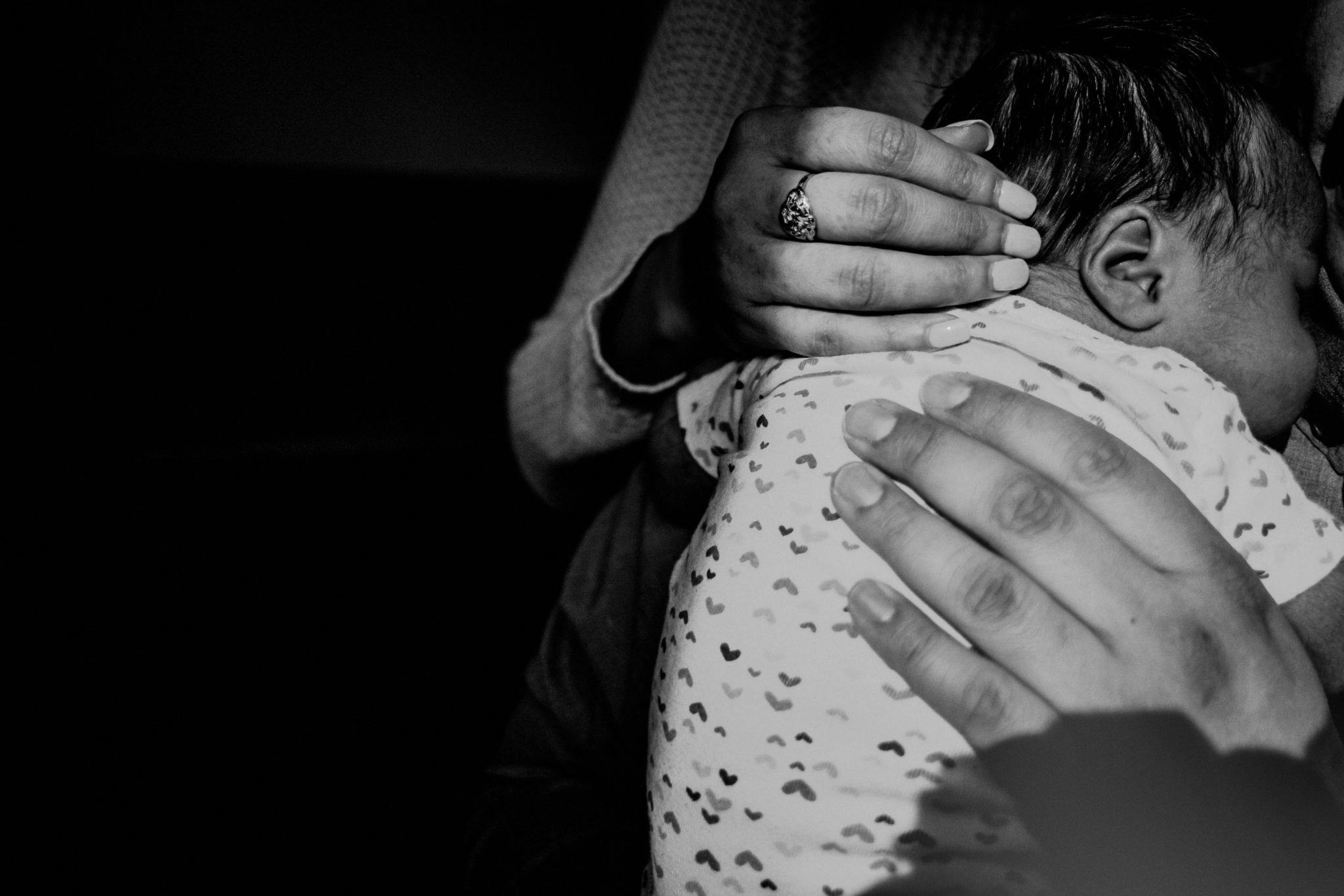 closeup of mother and father's hands on newborn baby, black and white photo