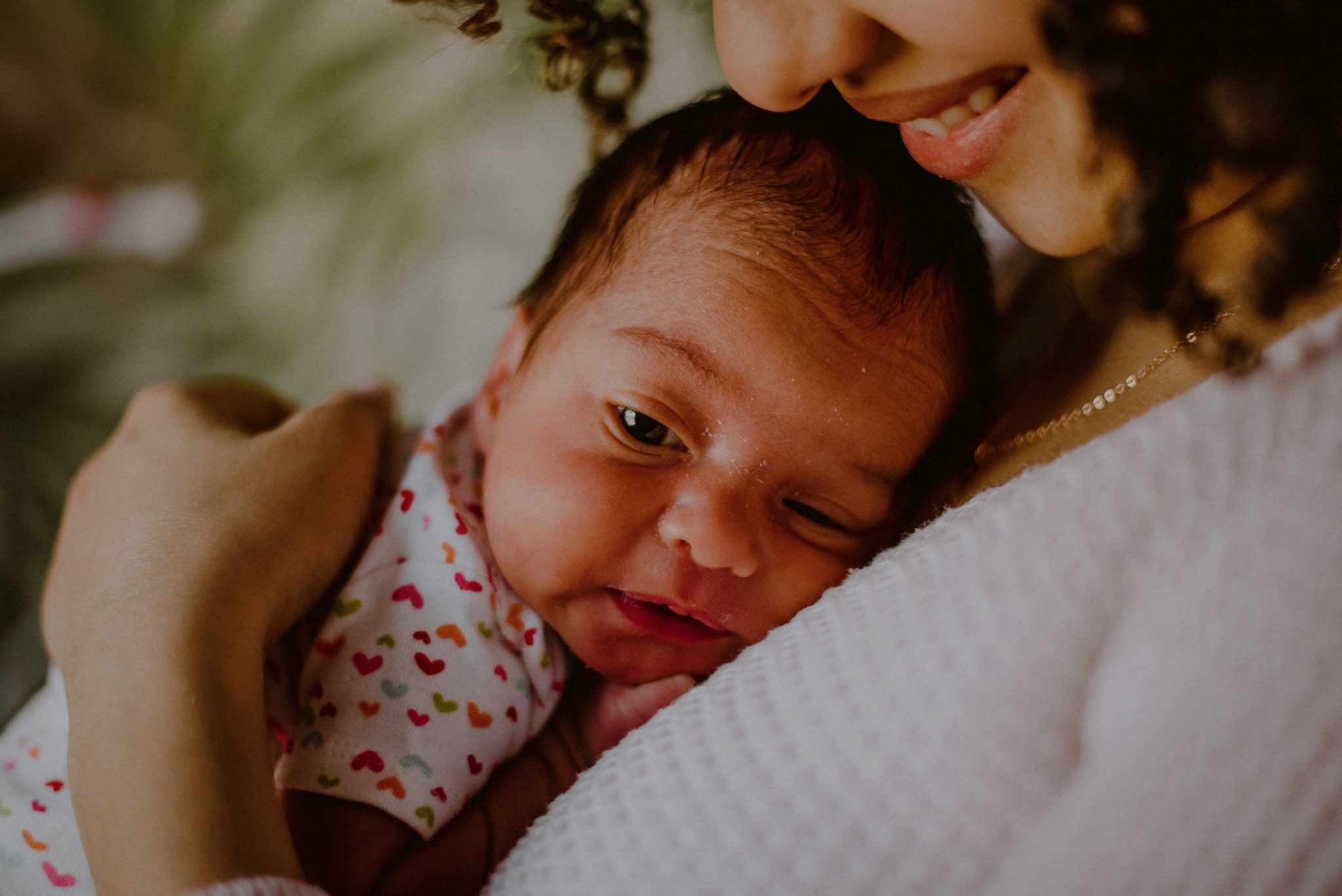 baby with eyes open on mother's chest while mom smiles