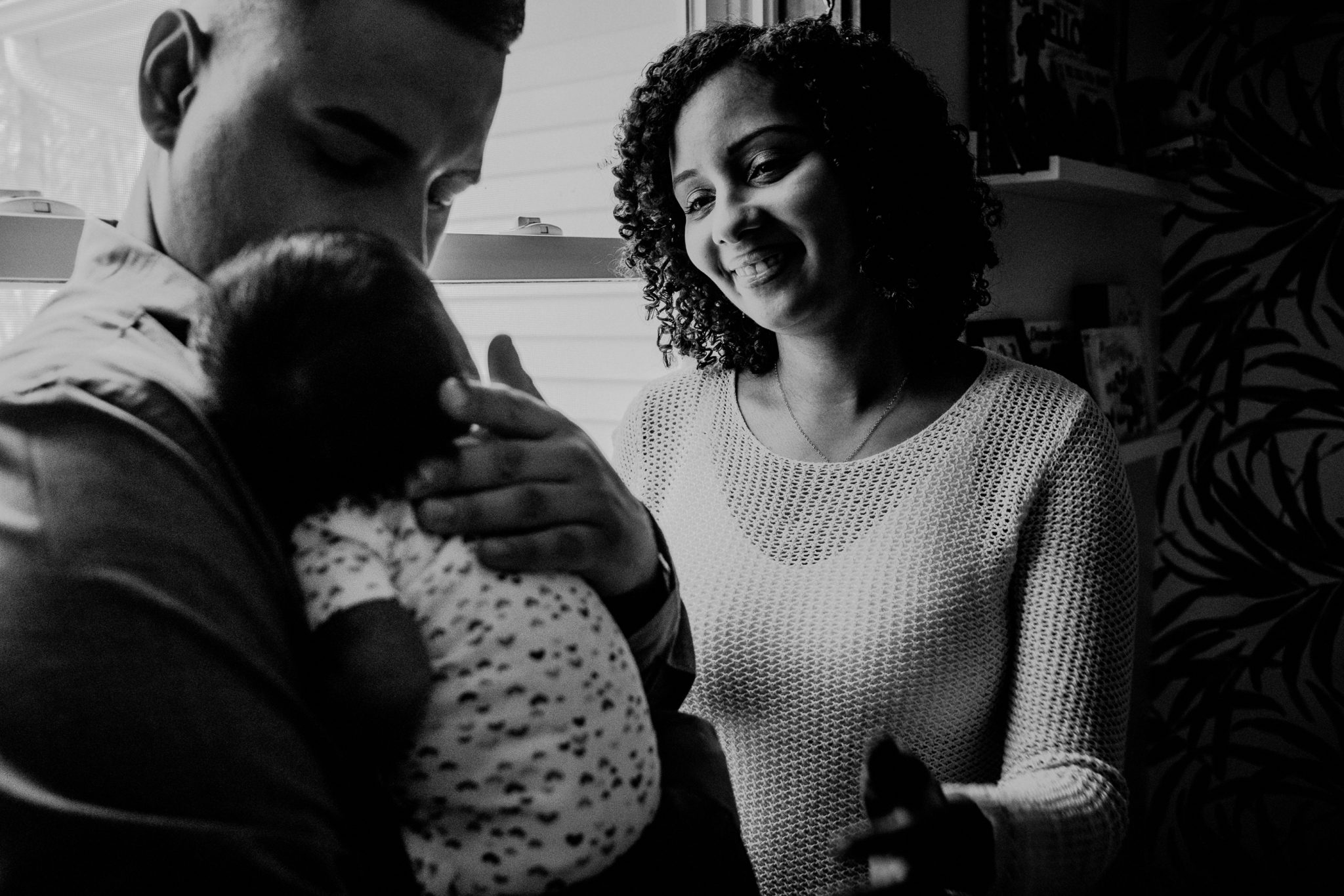 black and white photo of mother looking at newborn while father holds baby