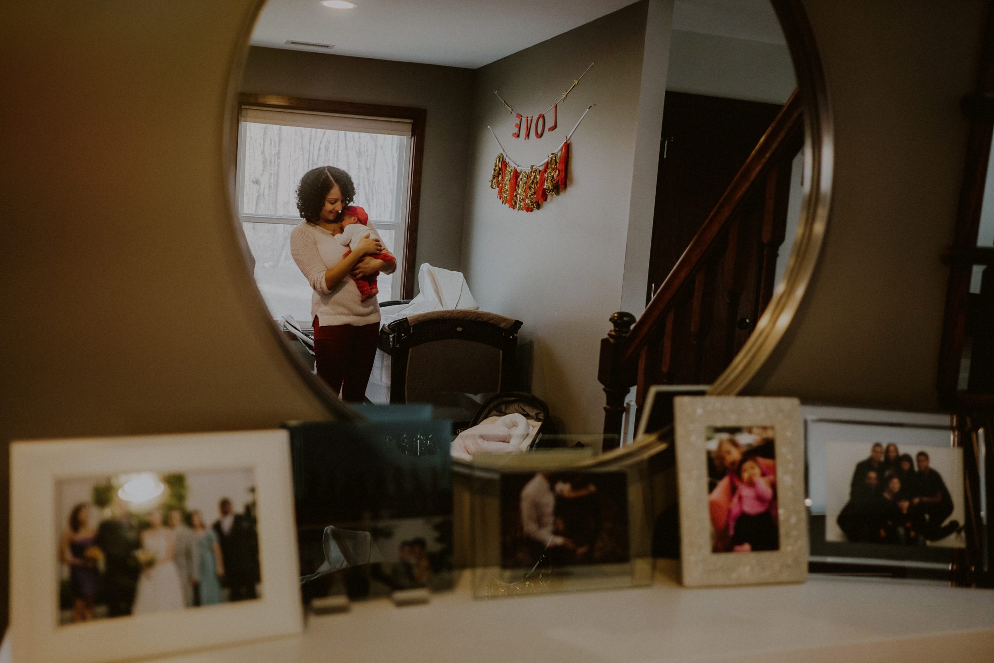 reflection of mother holding child in mirror, juxtaposed by printed family photos on counter