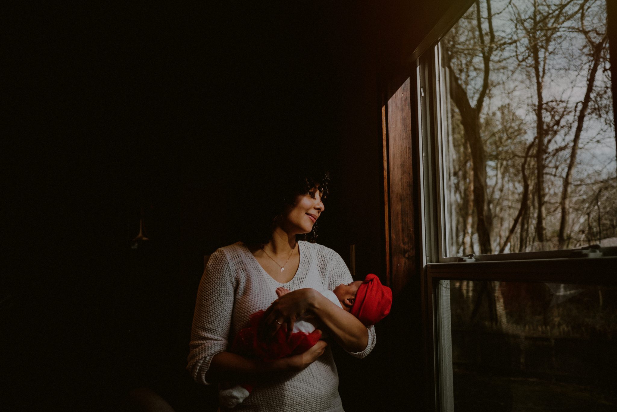 mother looking out window holding baby