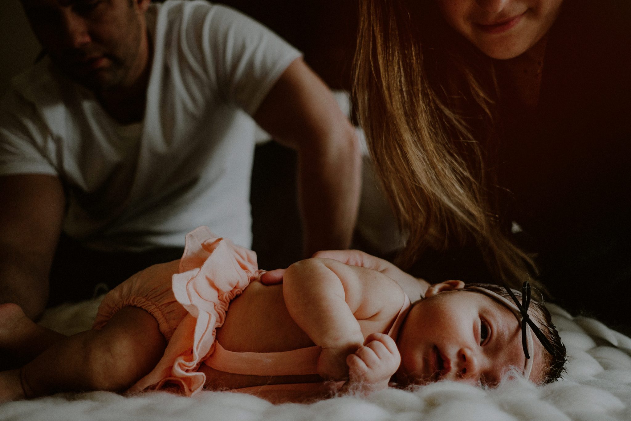 parents in background while baby lays for newborn portrait in foreground