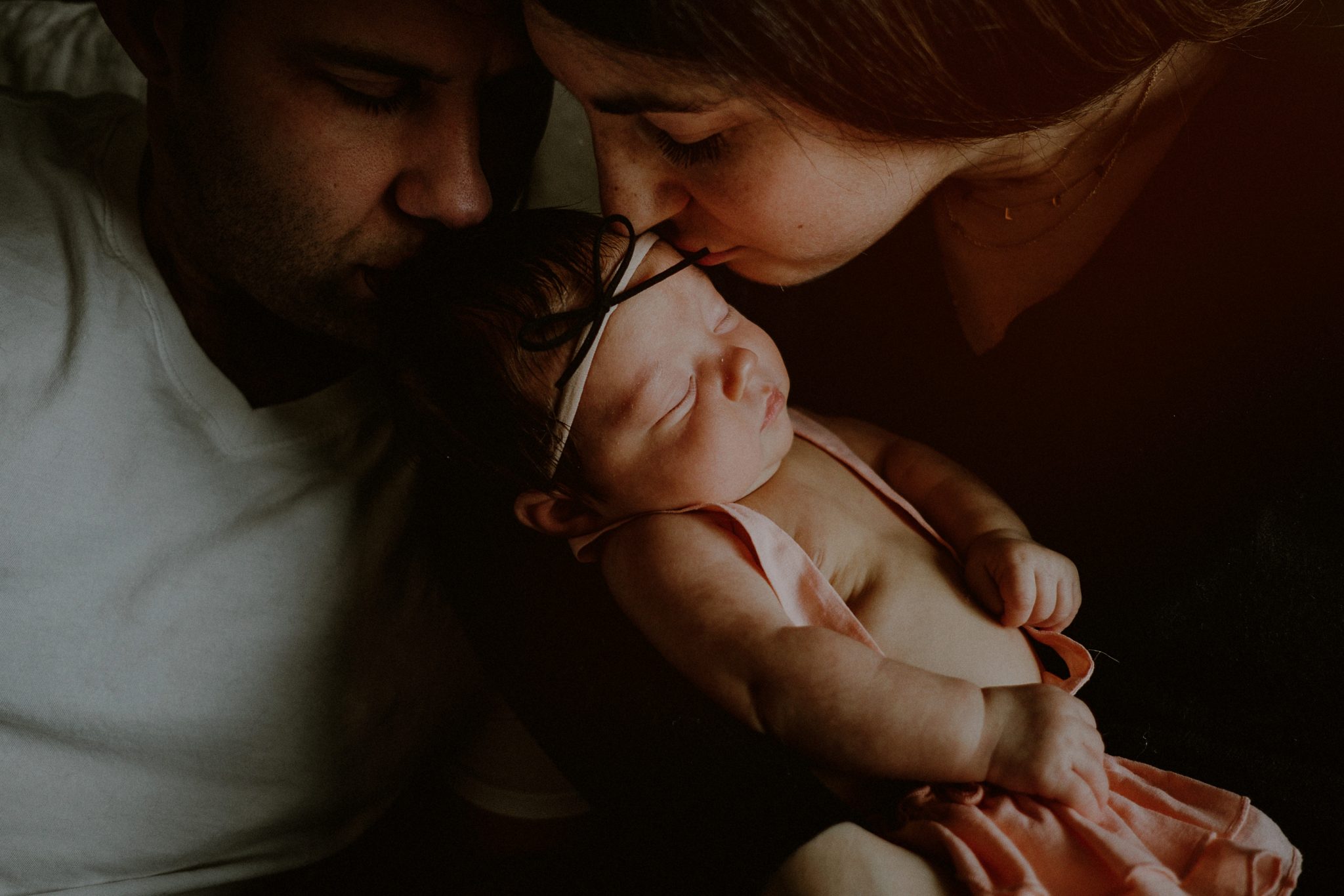 intimate family portrait of parents kissing baby's head