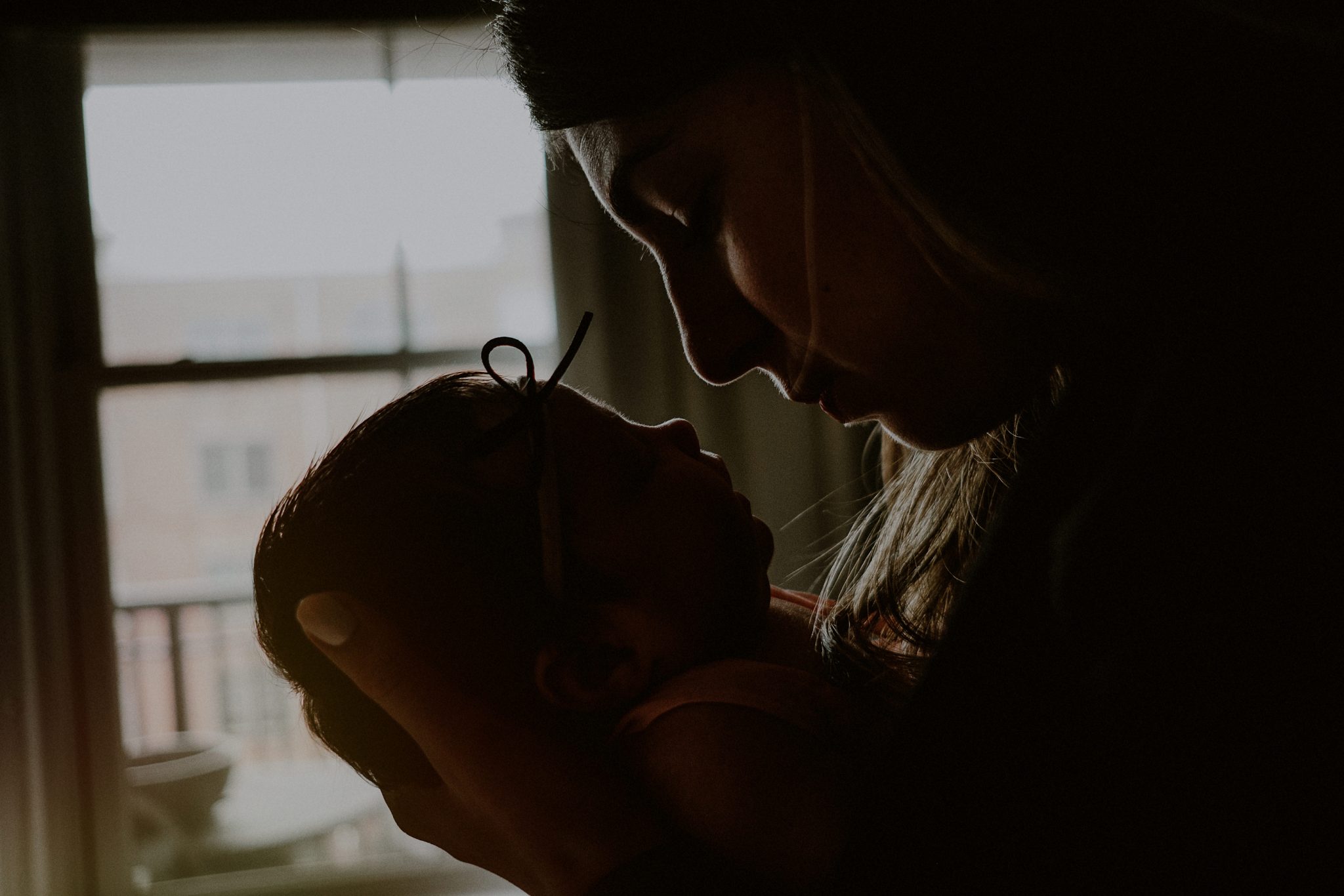 silhouette of mother's face holding baby's face by window