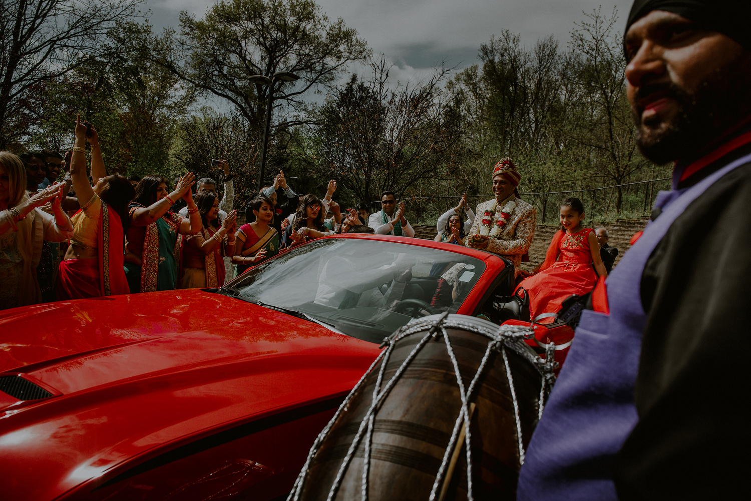 indian wedding photos of groom arriving in red corvette to baraat