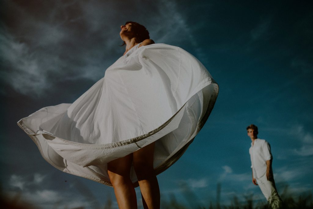 engaged couple posing wearing all white against blue sky