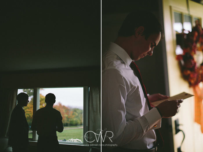 october wedding groom looking out window before ceremony with fall foliage