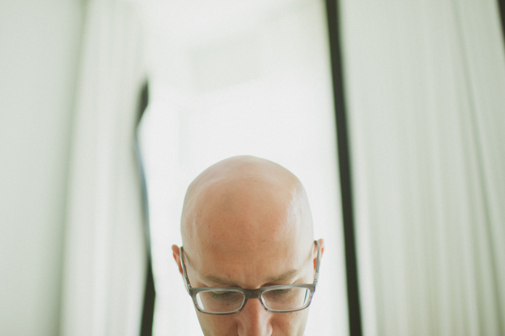 beach wedding photographer simple portrait of groom with bald head by window