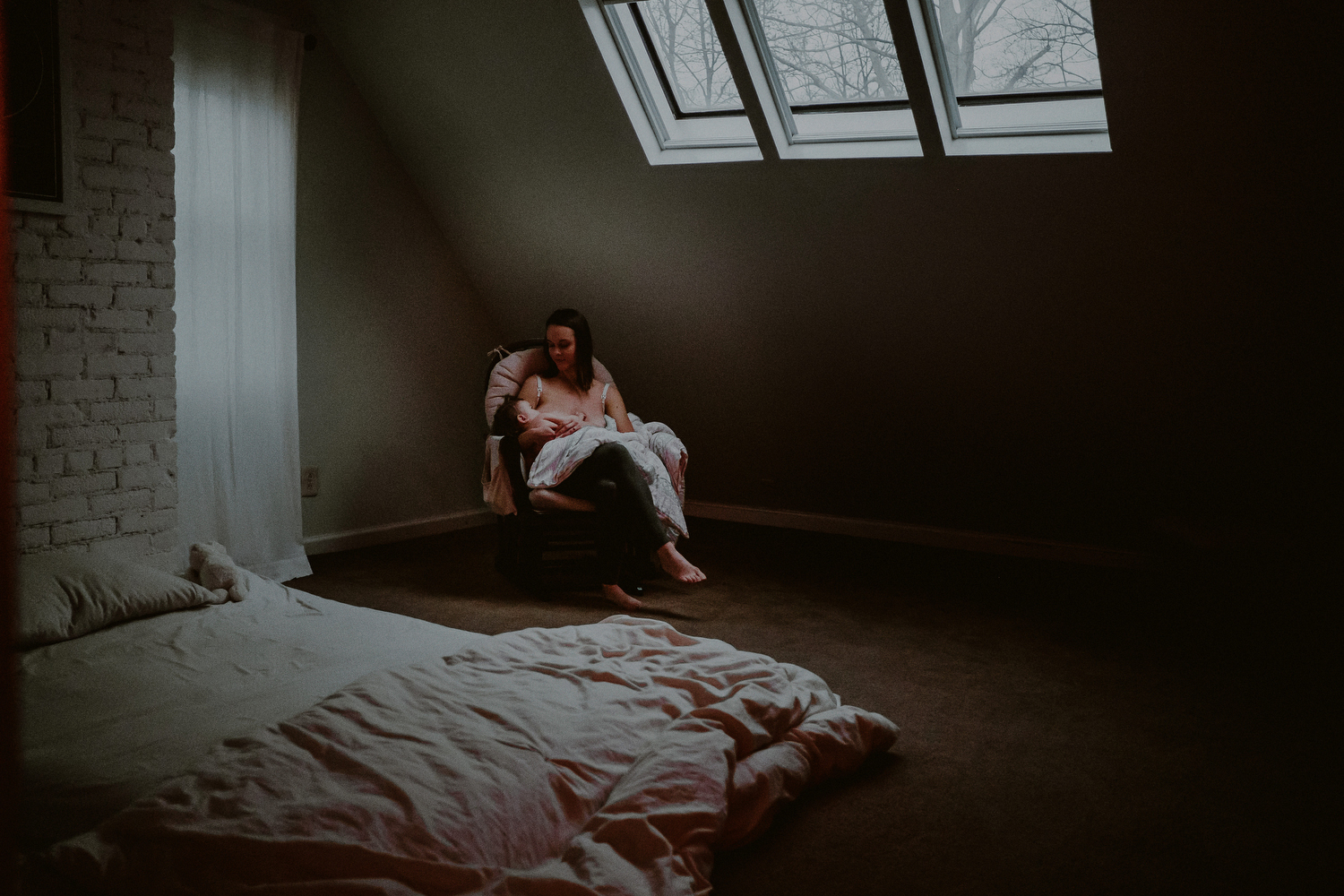 mother breastfeeding baby in bedroom under skylight during day in the life photo session