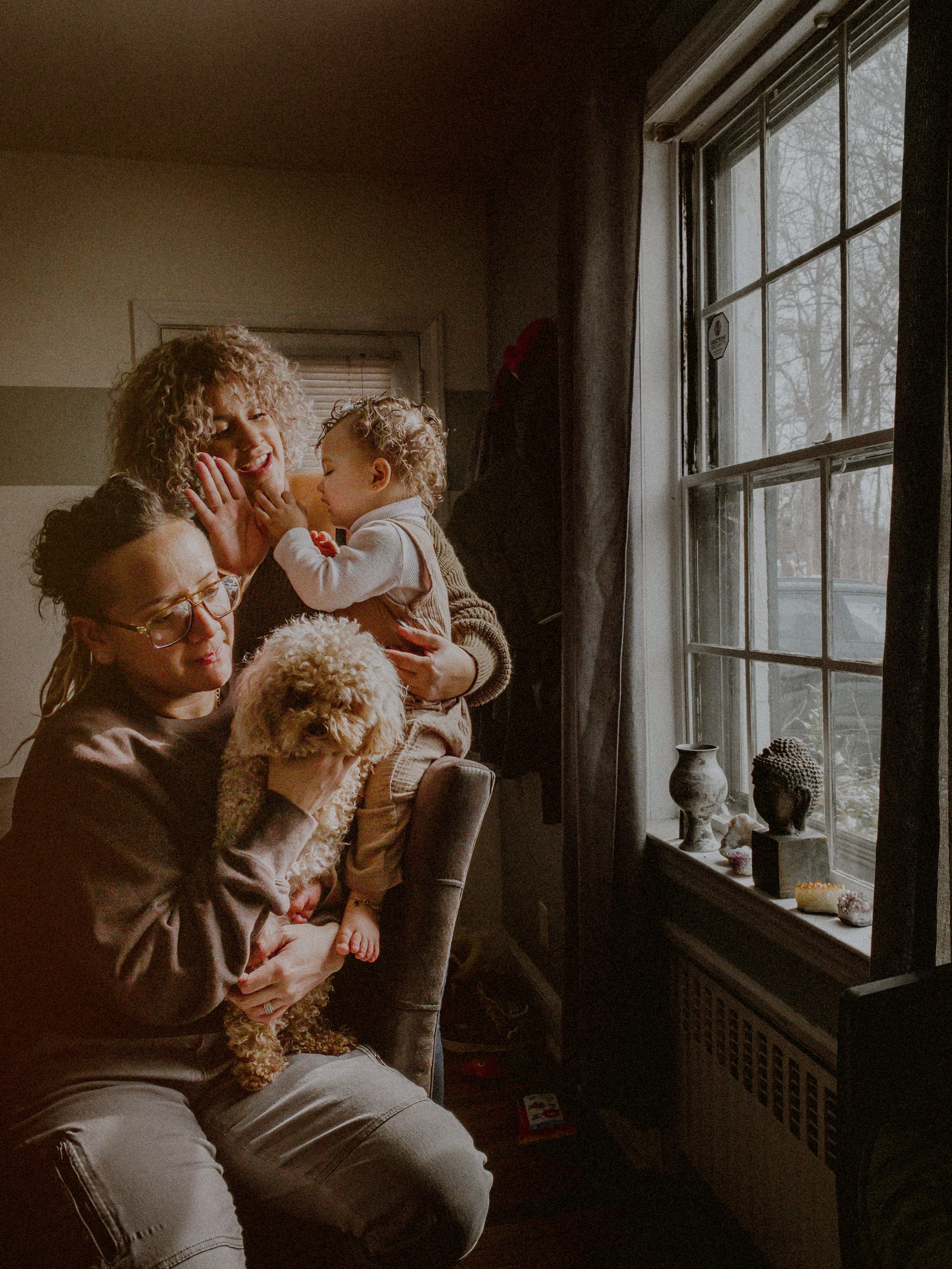 lgbtq family with daughter and dog posed by window