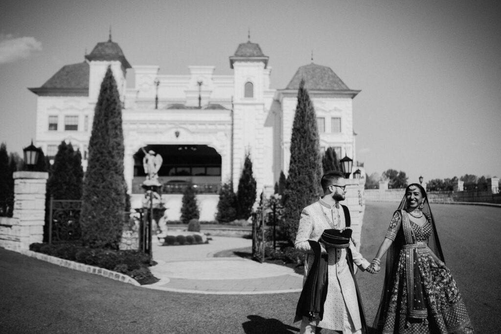 black and white image of wedding couple candidly walking away from luxurious wedding venue in background