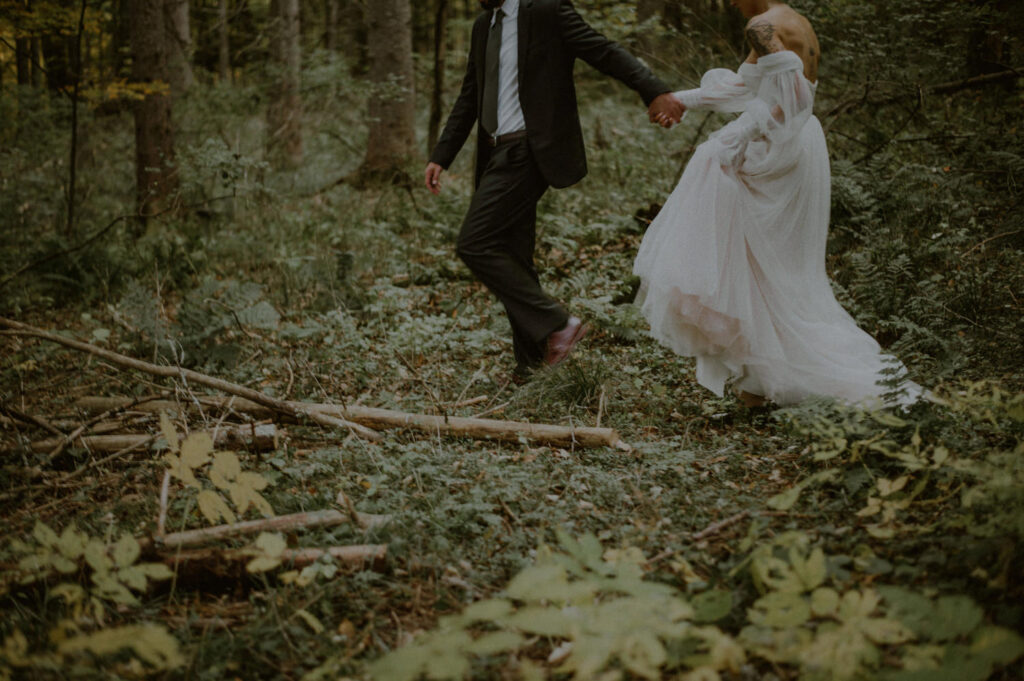 image of bride and groom walking together in the woods holding hands