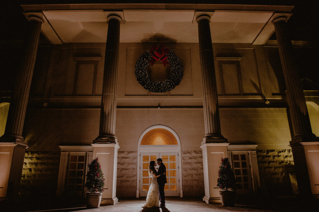 The Palace at Somerset Park - Luxury Wedding Venue in New Jersey - Bride and groom embracing in front of columns at entrance by Carolina Rivera