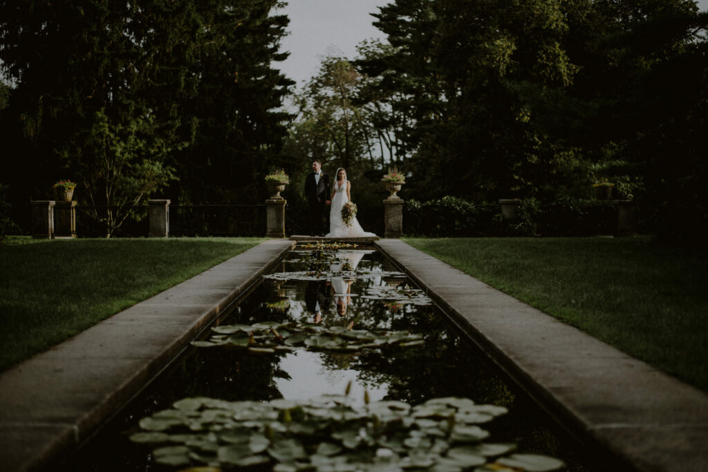 bride and groom posed in front of pond with reflection