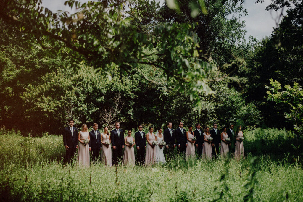 bridal party posing in the middle of a field at willowwood arboretum in a line