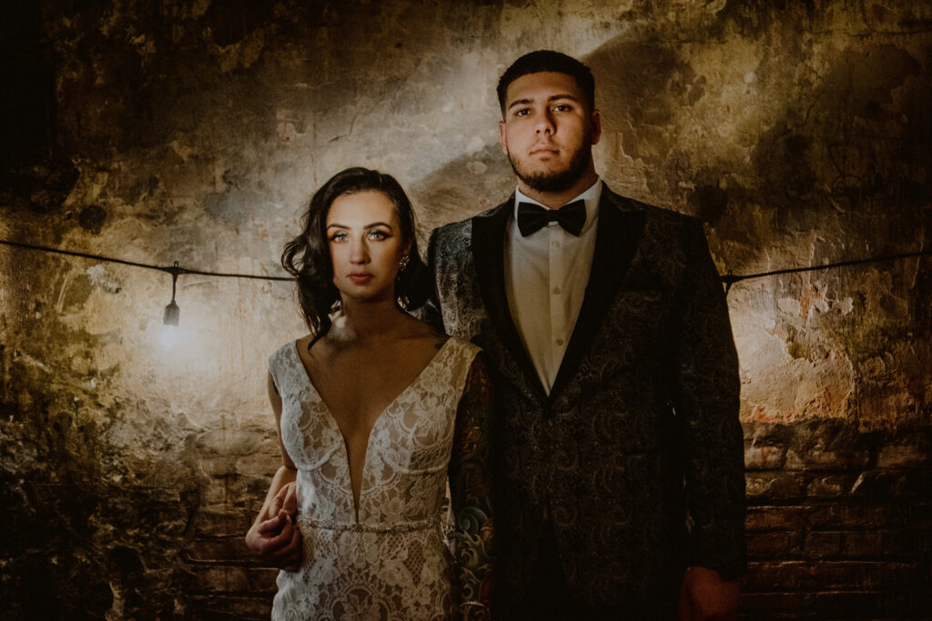 moody photo of bride and groom posed in dramatic lighting and grungy setting
