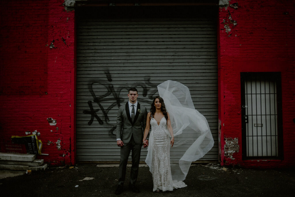 editorial wedding image of bride and groom in dramatic pose in front of an urban setting