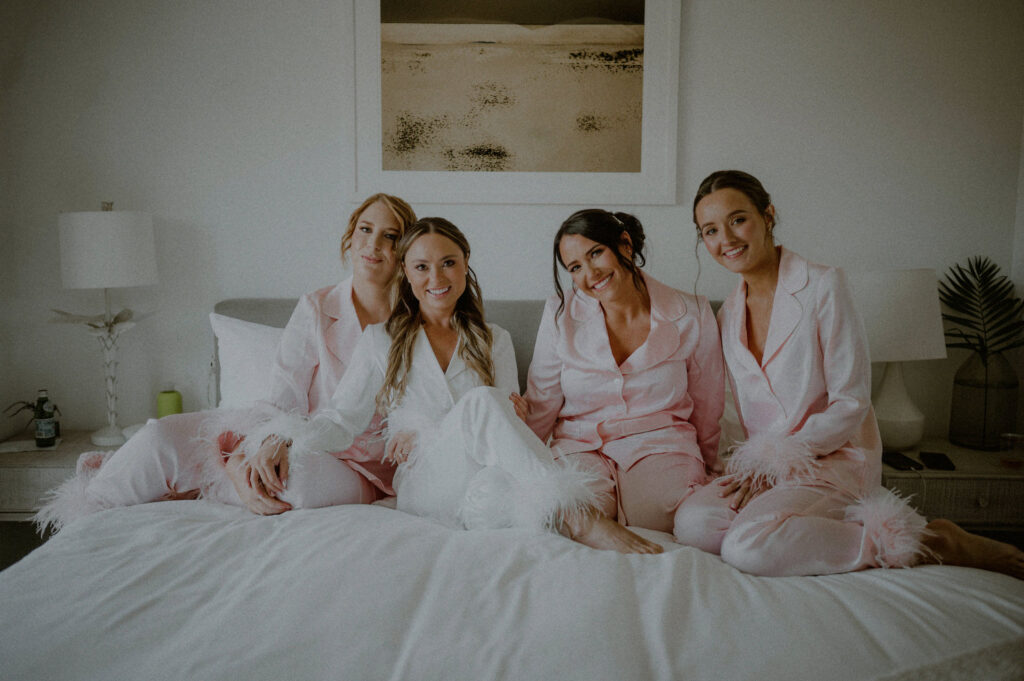 classic and playful photo of bridesmaids posing together on bed in robes and edited in a brighter light and airy style