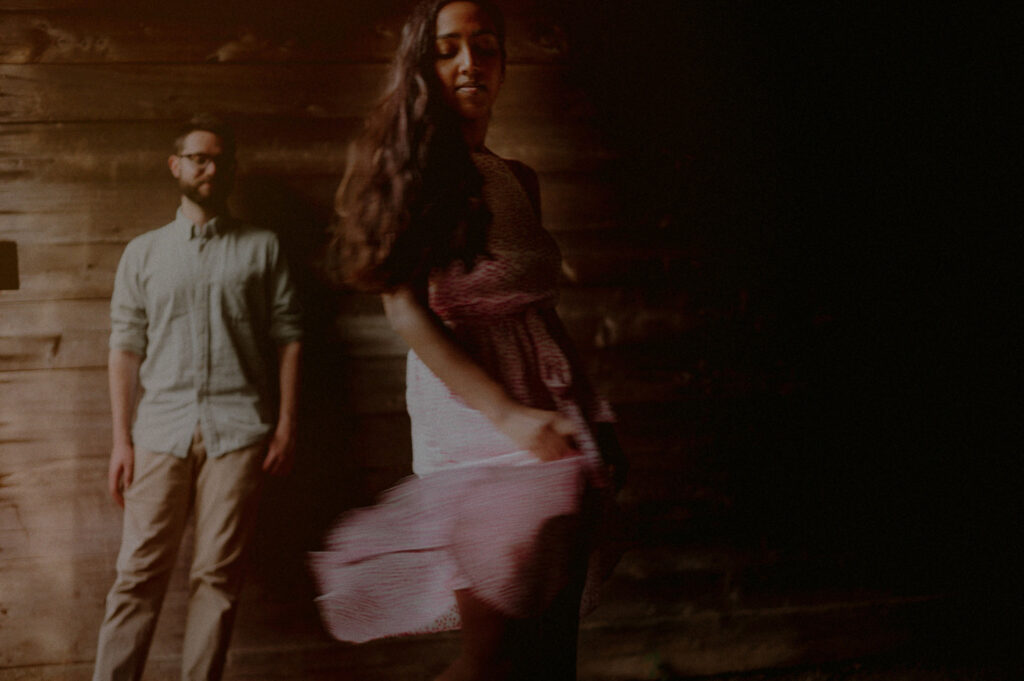 engagement photo of couple with woman in dress moving in foreground and man against the wall in the background 