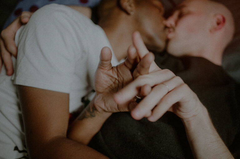 same sex couple kissing while laying down and playing with each other's hands