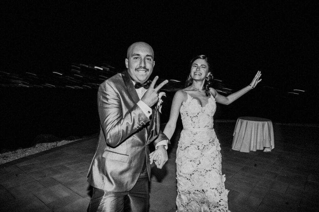 black and white photo of bride running towards camera giving peace sign