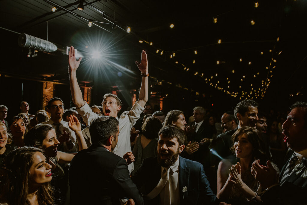 wedding guests singing and dancing at reception in dark industrial space