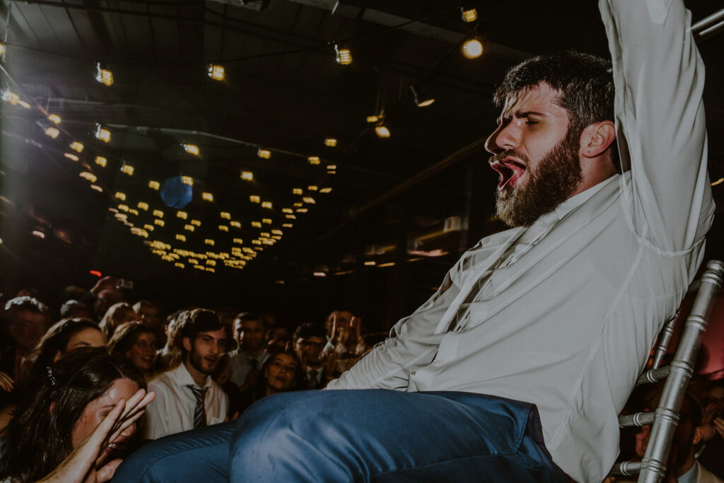 creative photo of groom lifted on chair and screaming during wedding reception