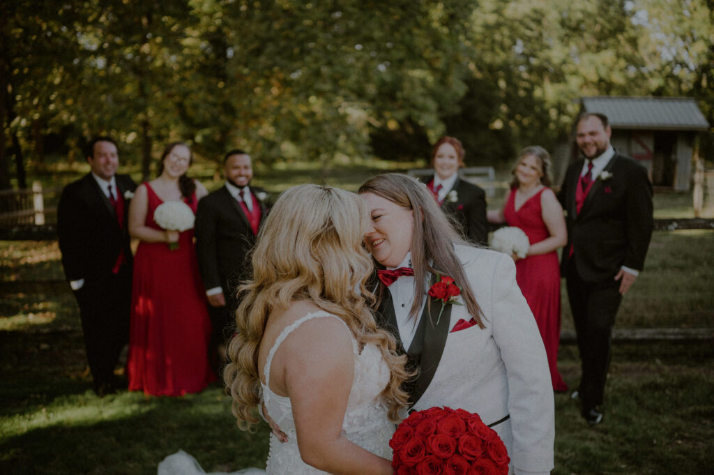 brides in foreground of image with wedding party in background dressed in red and black