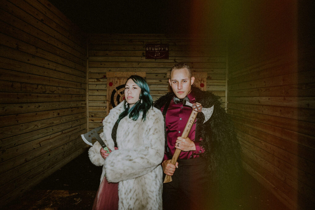 bride and groom alternatively dressed for their wedding and holding axes