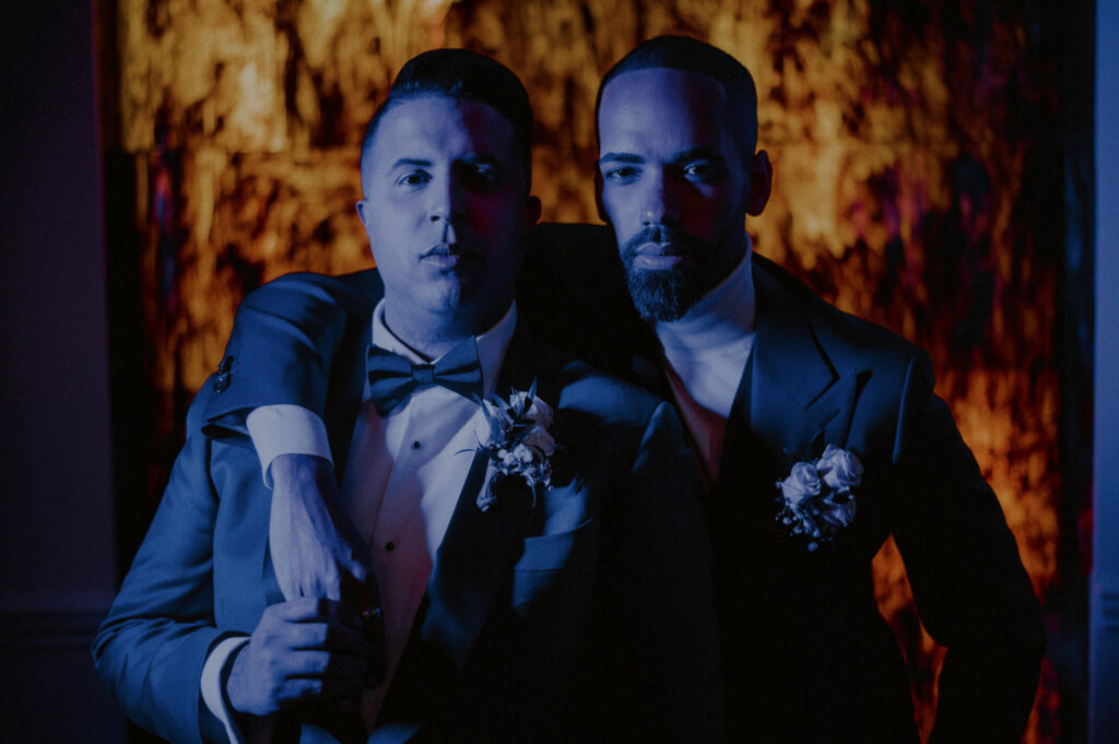 two grooms posed starkly in blue light with fire in background