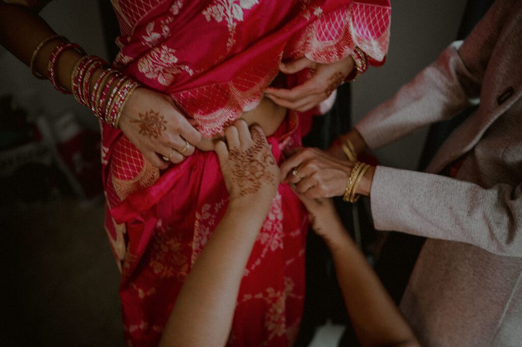 bride putting on sari as other hands enter the frame to help secure the clothing
