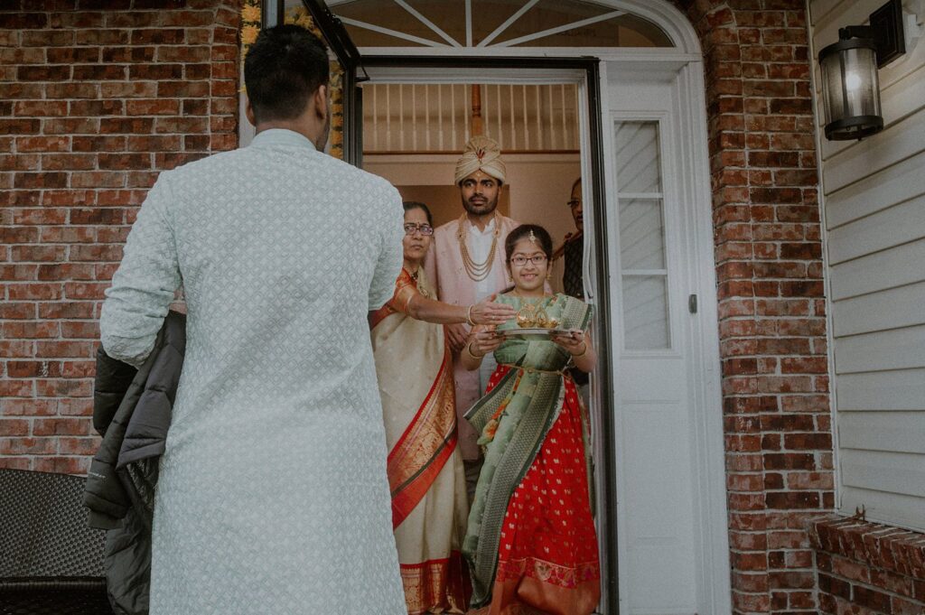 groom exiting home wearing turban and being lead by family