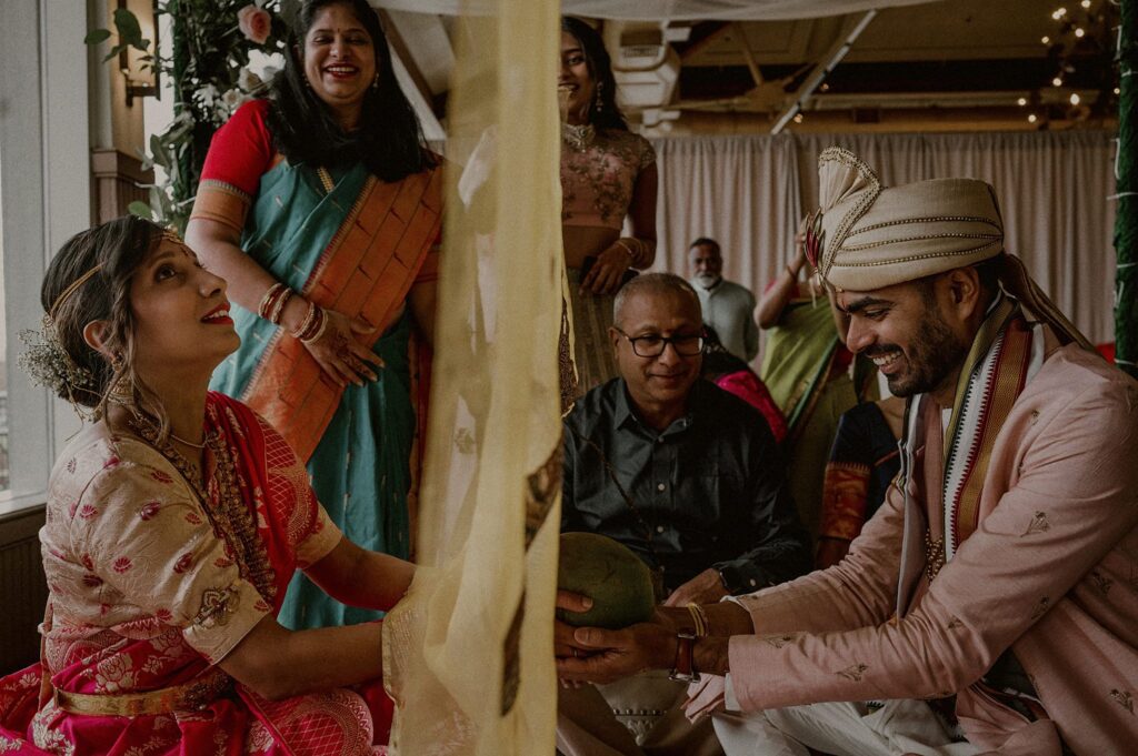 bride and groom laughing and separated by yellow sheet, while holding hands and coconut together