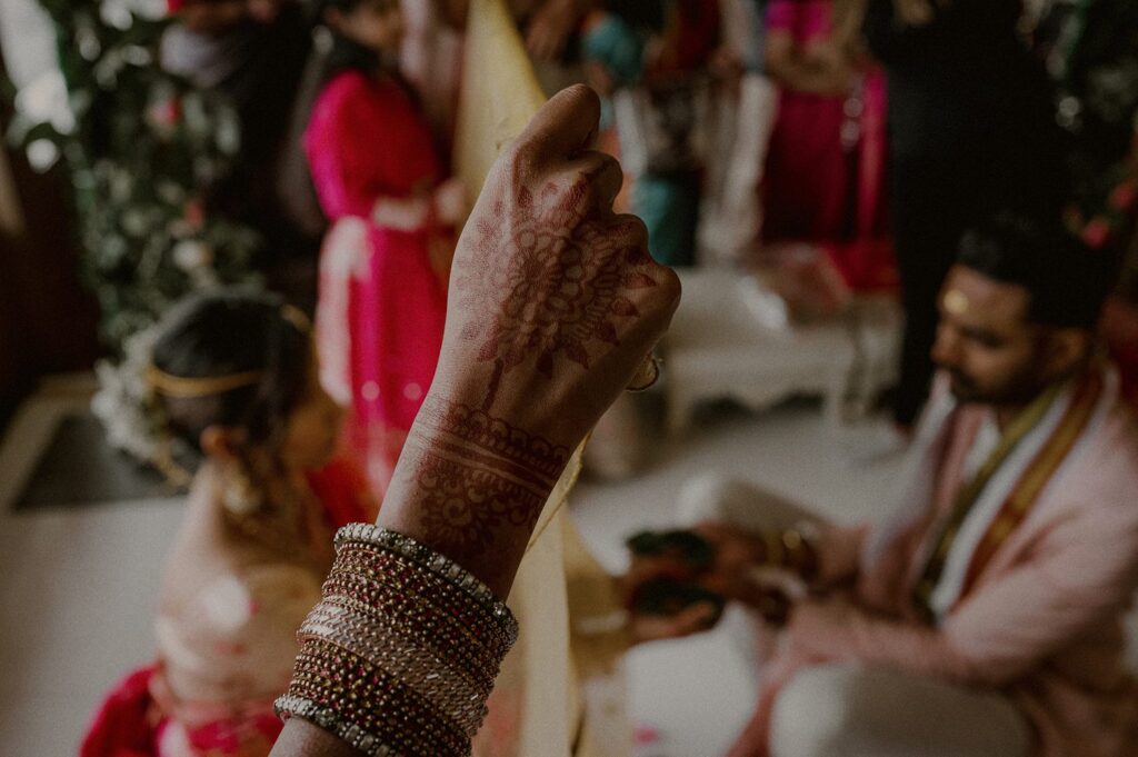 hand decorated in mehndi holding sheet up separating bride and groom in background 