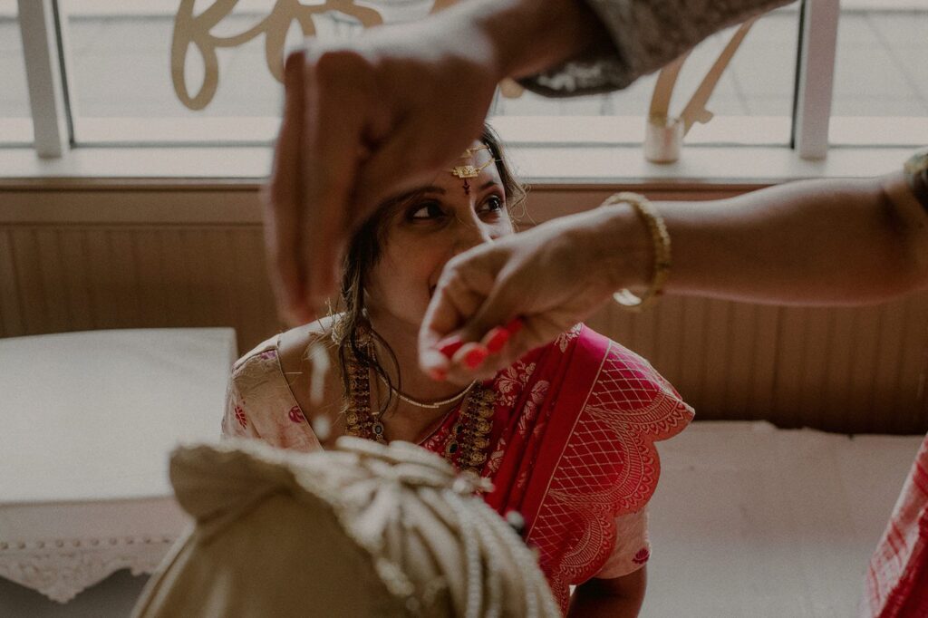 bride's face framed by hands pouring rice on groom's head