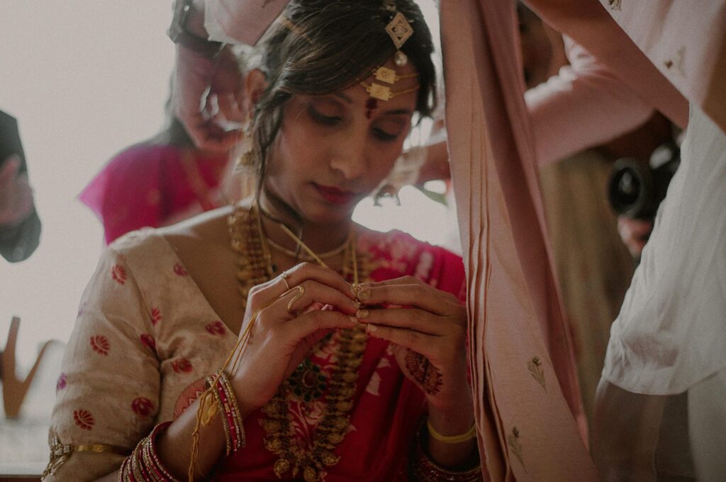 indian bride holding necklace as groom clasps it on in the back