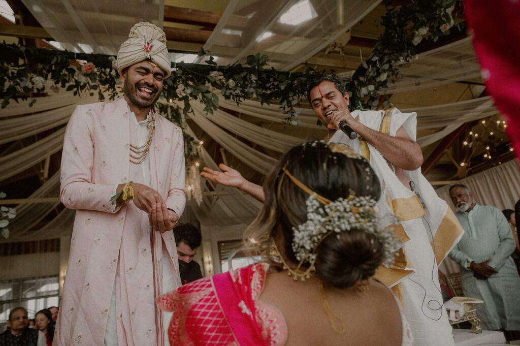 groom laughing as he is throwing rice grains at bride in traditional indian wedding rituals