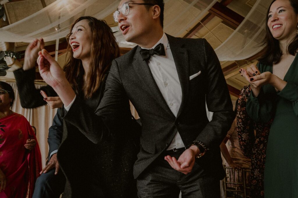 wedding guests laughing as they participate in indian wedding ceremony rice throwing