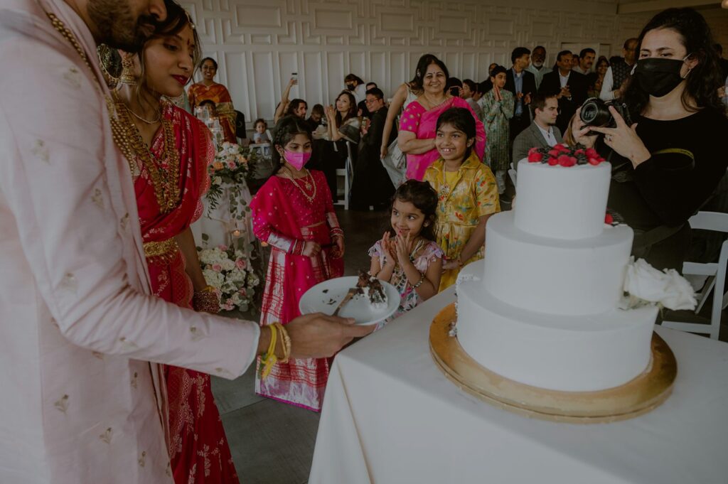 candid moment as children look at bride and groom cutting their wedding cake