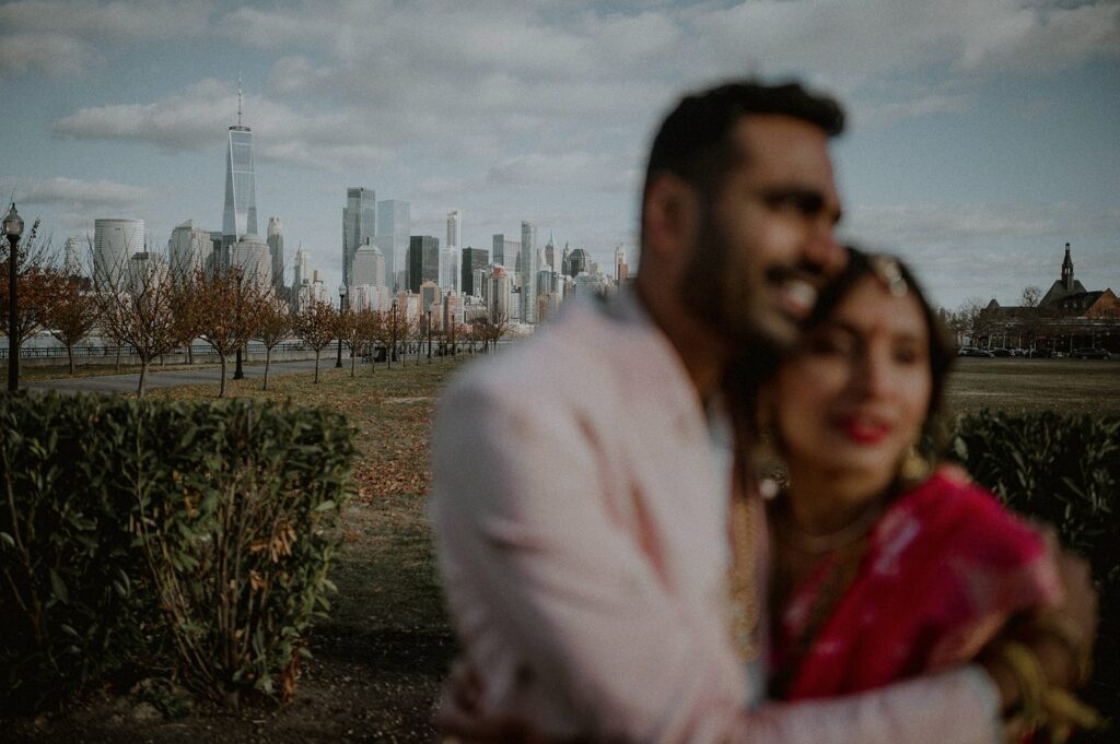 out of focus portrait of bride and groom hugging in foreground with in-focus skyline in the background