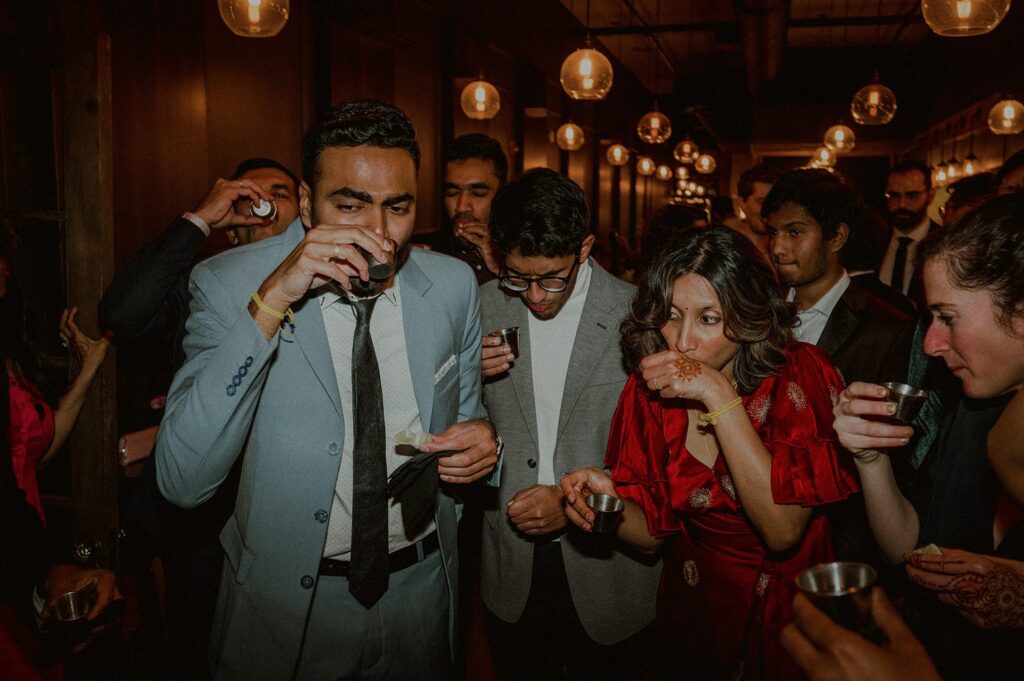 bride and groom taking tequila shots and surrounded by guests at restaurant wedding reception