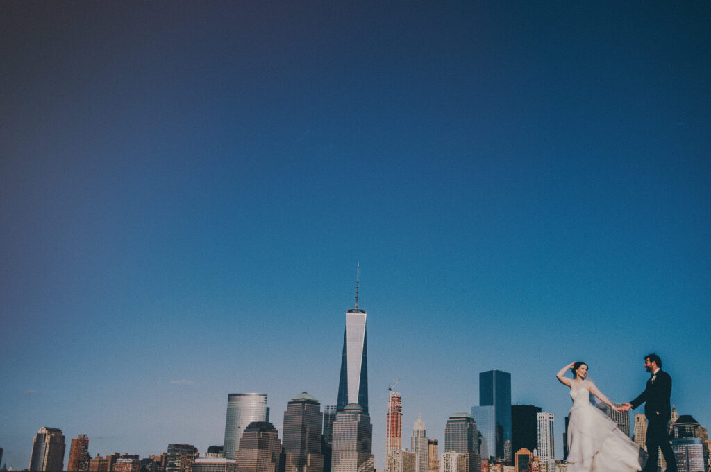 bride and groom walking in front of nyc skyline 