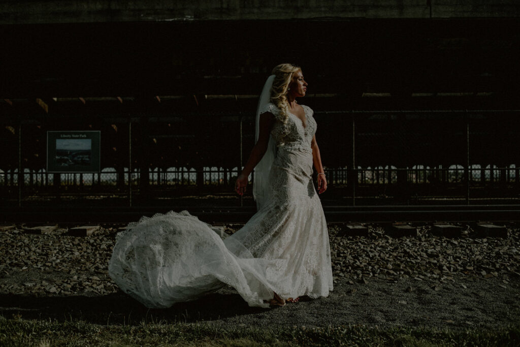 bride posing in dark and moody vibe in front of train tracks at liberty state park