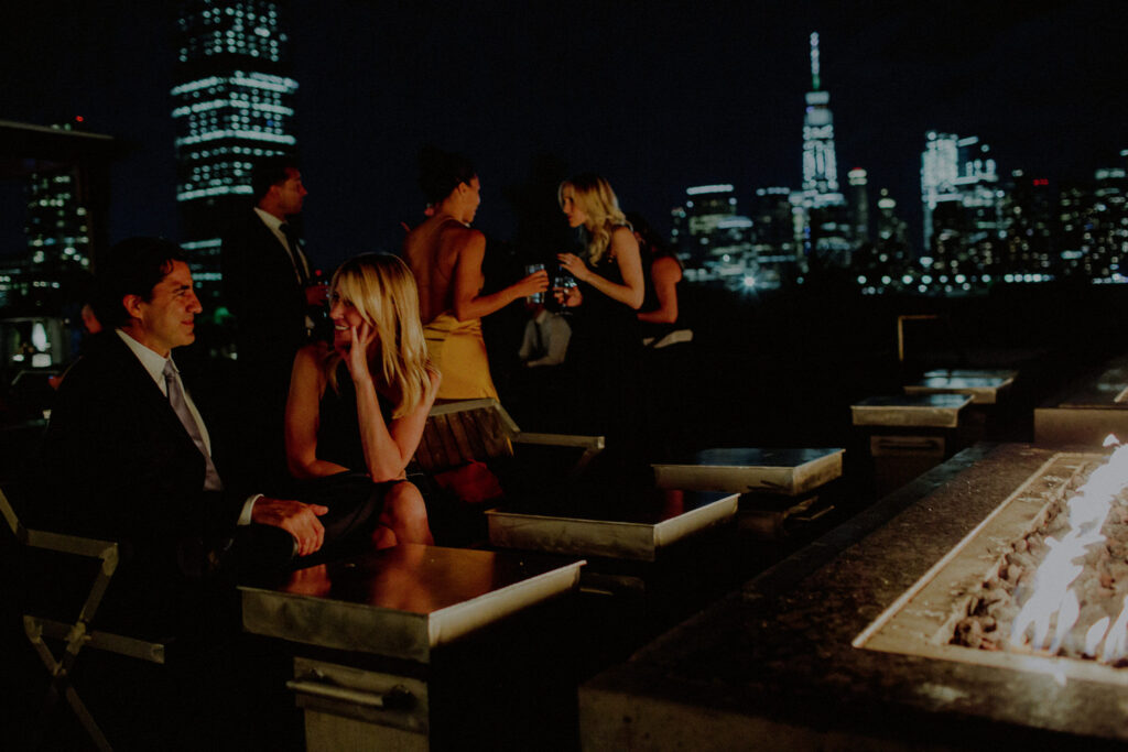 guests mingling at night outside of firepit with nyc buildings lit up in the background