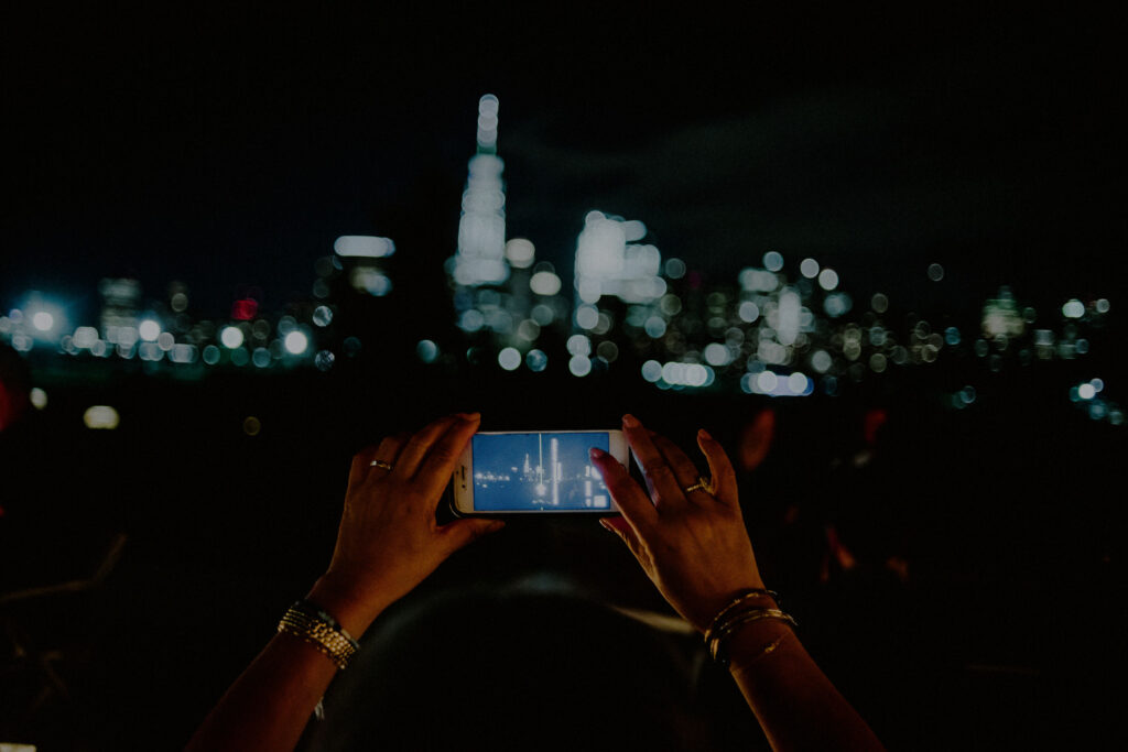 hands with an iphone taking photo of the nyc skyline at night