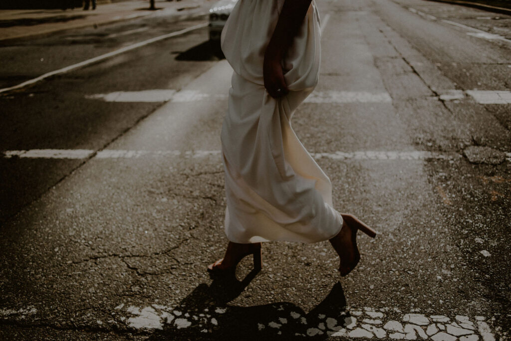 bride pulling up dress and walking on the road with her high heels