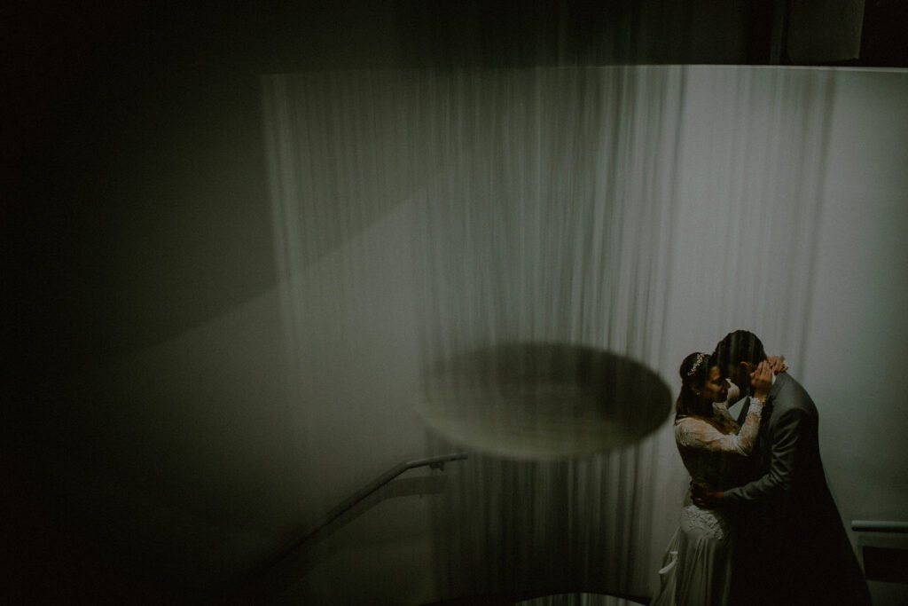 bride and groom romantically embraced in front of modern chandelier