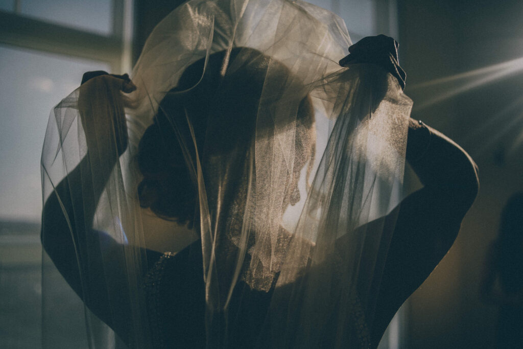 bride putting on her veil with a flair of sunlight behind her